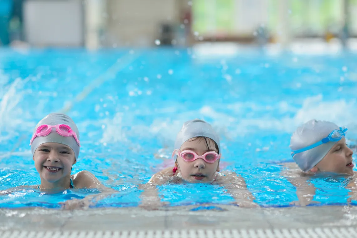 3 kids practicing kicks in the pool