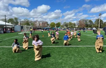 large group of children racing in potato sacs jumping toward the camera