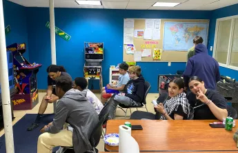 teens hanging out at teen center playing video games, watching sports, and smiling