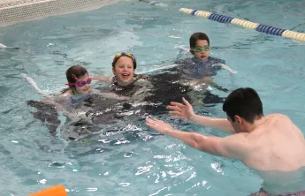 3 participants with swim instructor in the pool during class