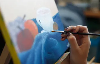 a hand holding a paintbrush in front of a painting