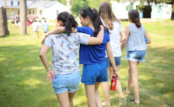 Two girls walking across a grassy field with their arms draped over each other