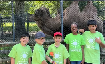 camp pikati campers pose in front of a camel at the zoo