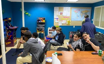 teens hanging out at teen center playing video games, watching sports, and smiling