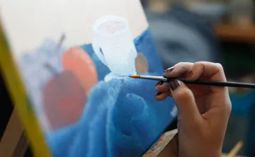 a hand holding a paintbrush in front of a painting