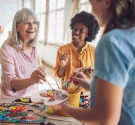 People standing around a table with paint brushes, dipping them into a palette.