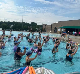 Several people in a pool with their hands in the air as they perform aqua fitness moves.