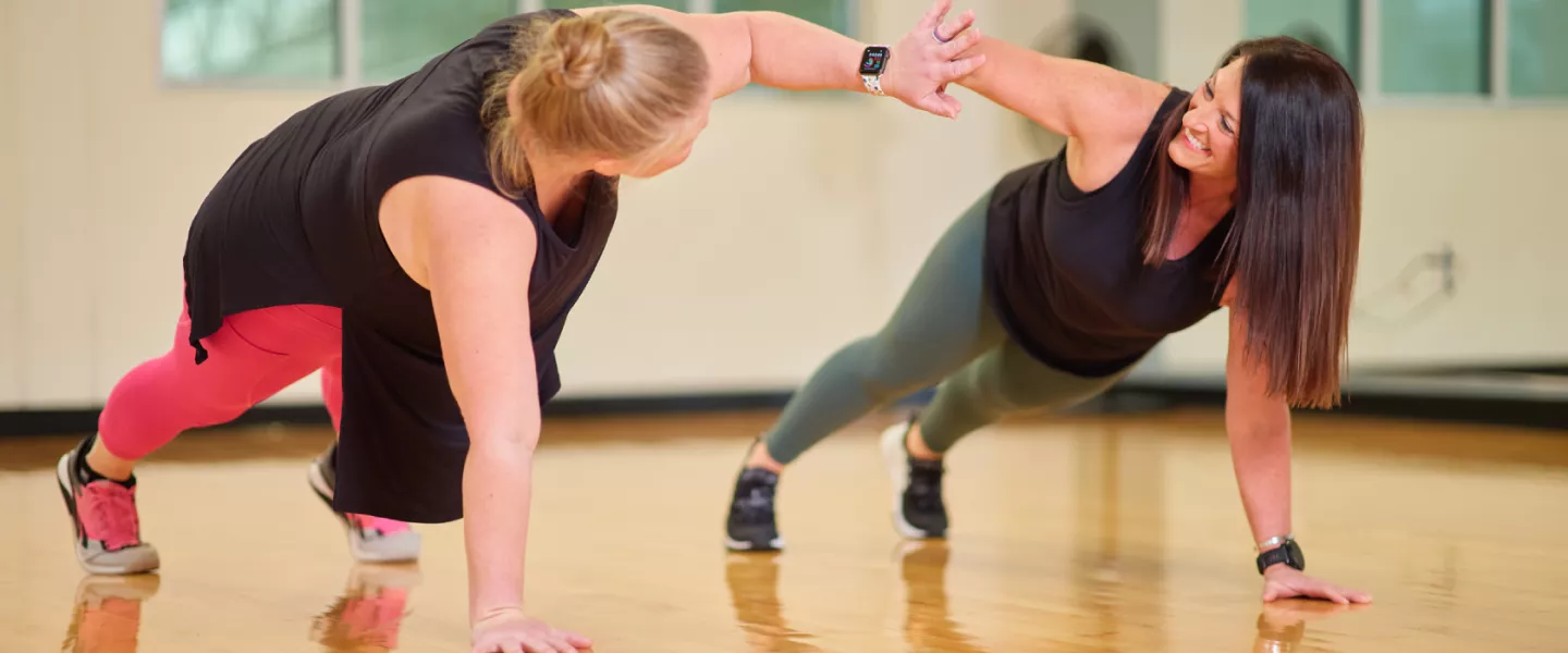 Two women in plank position give each other a high five at the YMCA