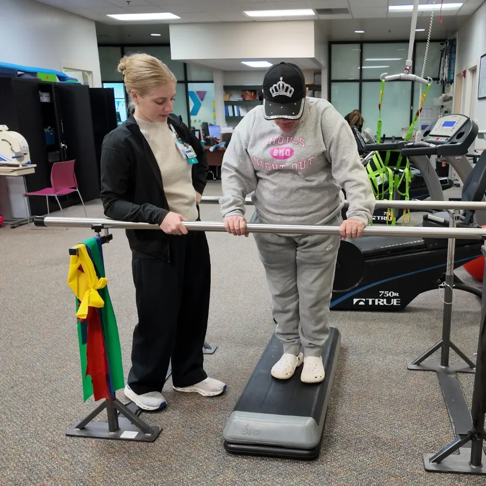 A physical therapist guides a client on a step.