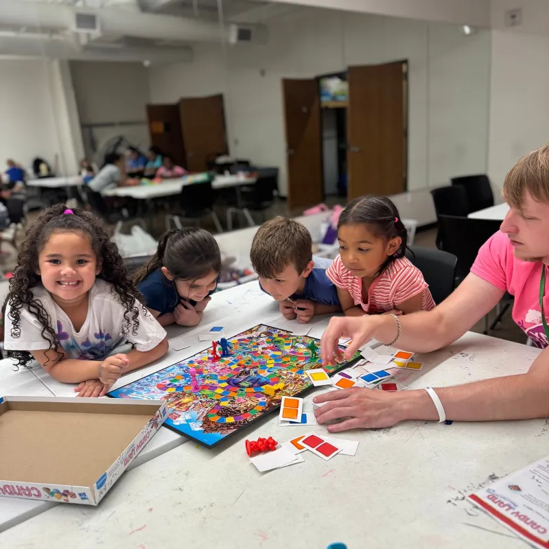 A group of kids play a board game with a youth development employee.