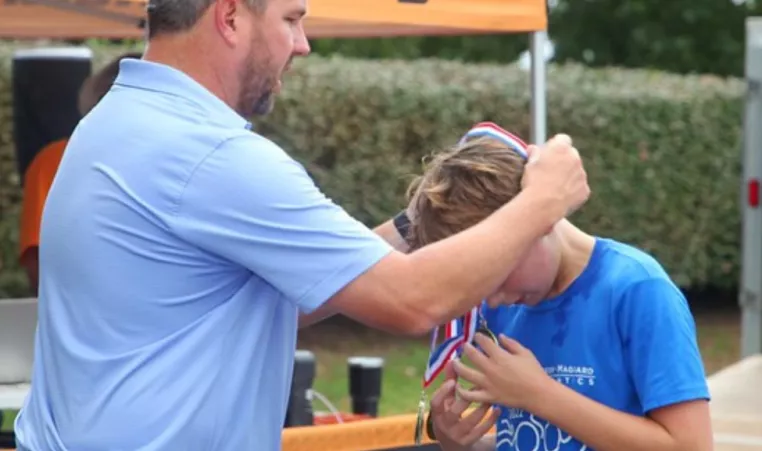 Dr. Cliff from WGM presents an athlete with a medal at the White, Greer & Maggard Kids Tri at the YMCA of Central KY.