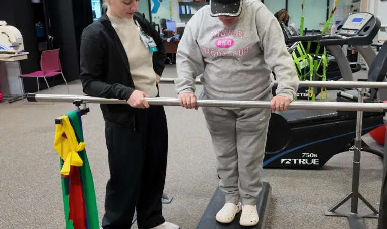 A physical therapist guides a client on a step.