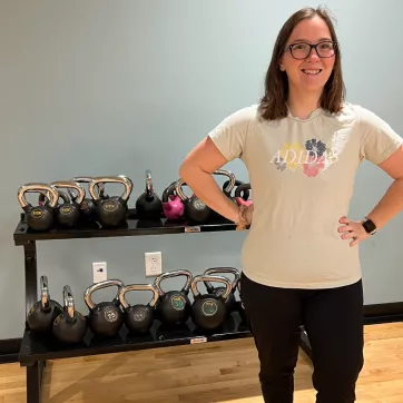 Member Lacy smiles next to the kettlebell stand at the Whitaker Family YMCA.