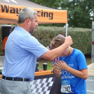 Dr. Cliff from WGM presents an athlete with a medal at the White, Greer & Maggard Kids Tri at the YMCA of Central KY.