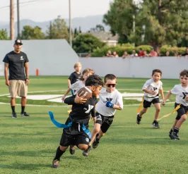 Young athlete running with a football during a flag football game