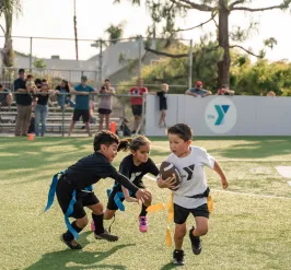 Child running with the football as the opposing team tries to pull his flags