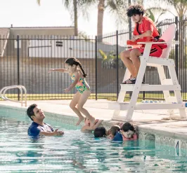 Child jumping into the water with lifeguard and swim instructor looking on