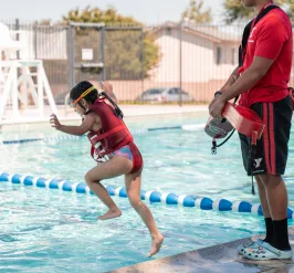 Child with life vest jumping into the pool with a lifeguard closely watching