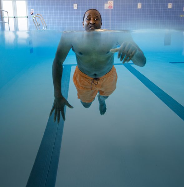 Man in pool where the reflection of the water makes his body much larger in comparison to his head, which is above the water.