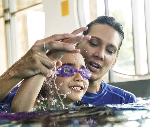 A Y swim instructor teaches a smiling child to do the forward crawl swim stroke