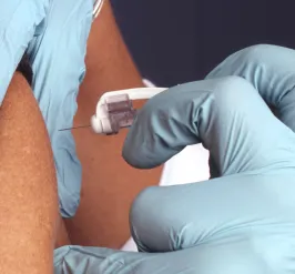 gloved hands administering a vaccine into a person's arm with a needle