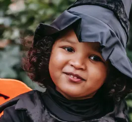 a young child dressed as a witch and standing by halloween decorations