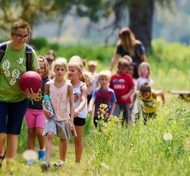 camp counselor leads campers through a field to tall grass