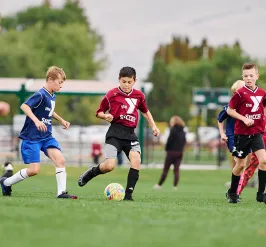 boys in red and blue jerseys play a soccer game outside on green grass
