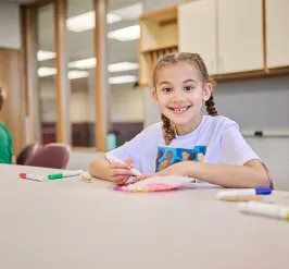 Girl smiling wearing white shirt holding a marker coloring 