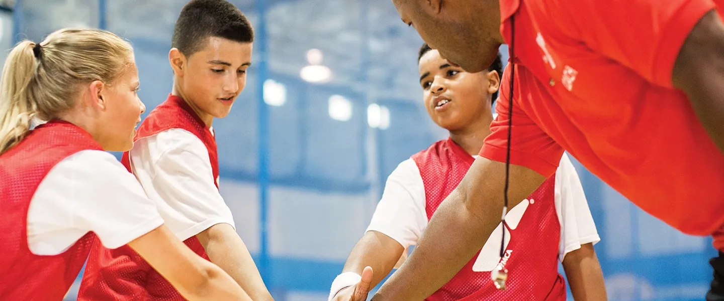 children in basketball jerseys and their coach putting their hands together for a cheer