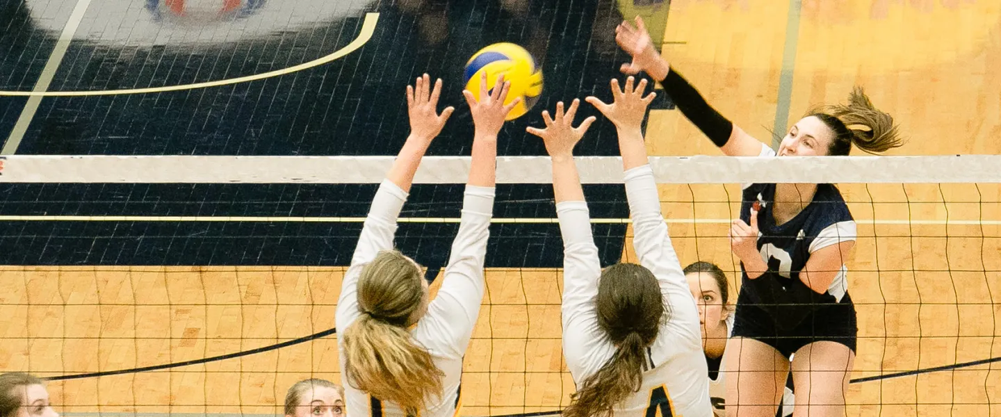 teenage volleyball players reaching over a net for a volleyball