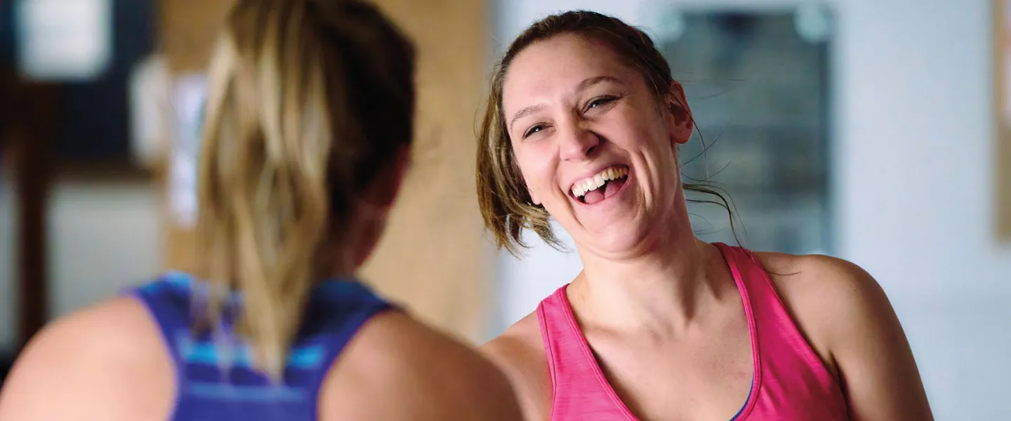 two adults in workout clothes laugh together after a fitness class