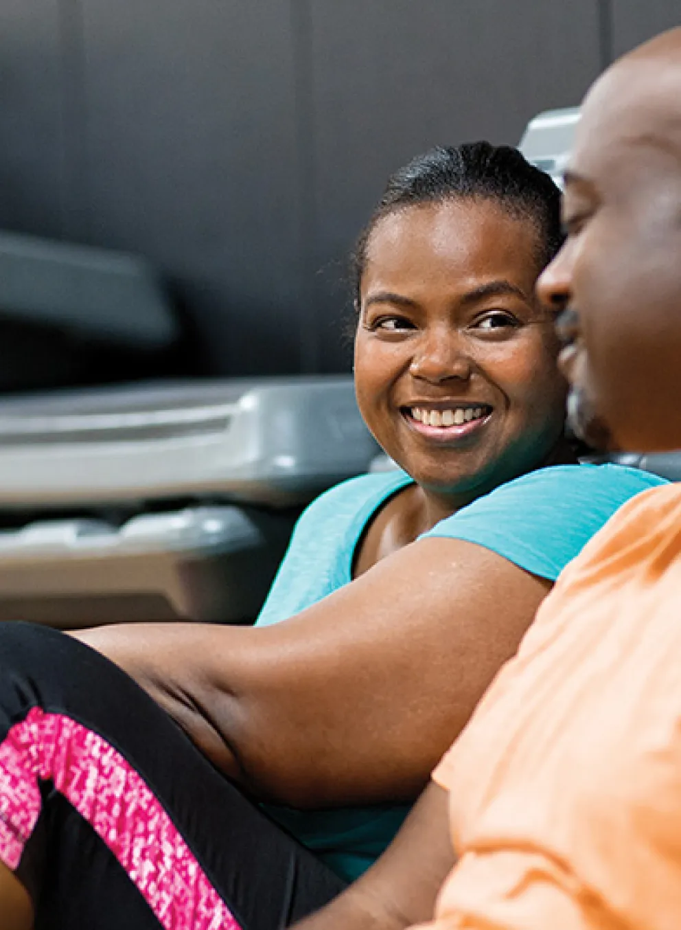 two adults in fitness clothes sitting on the ground in front of exercise equipment