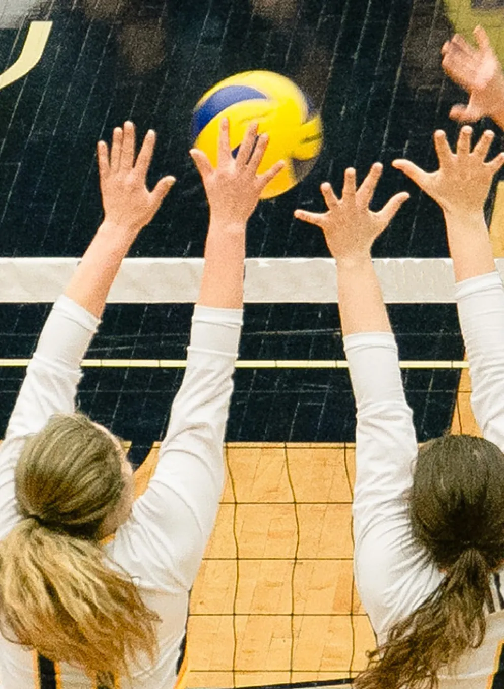 teenage volleyball players reaching over a net for a volleyball