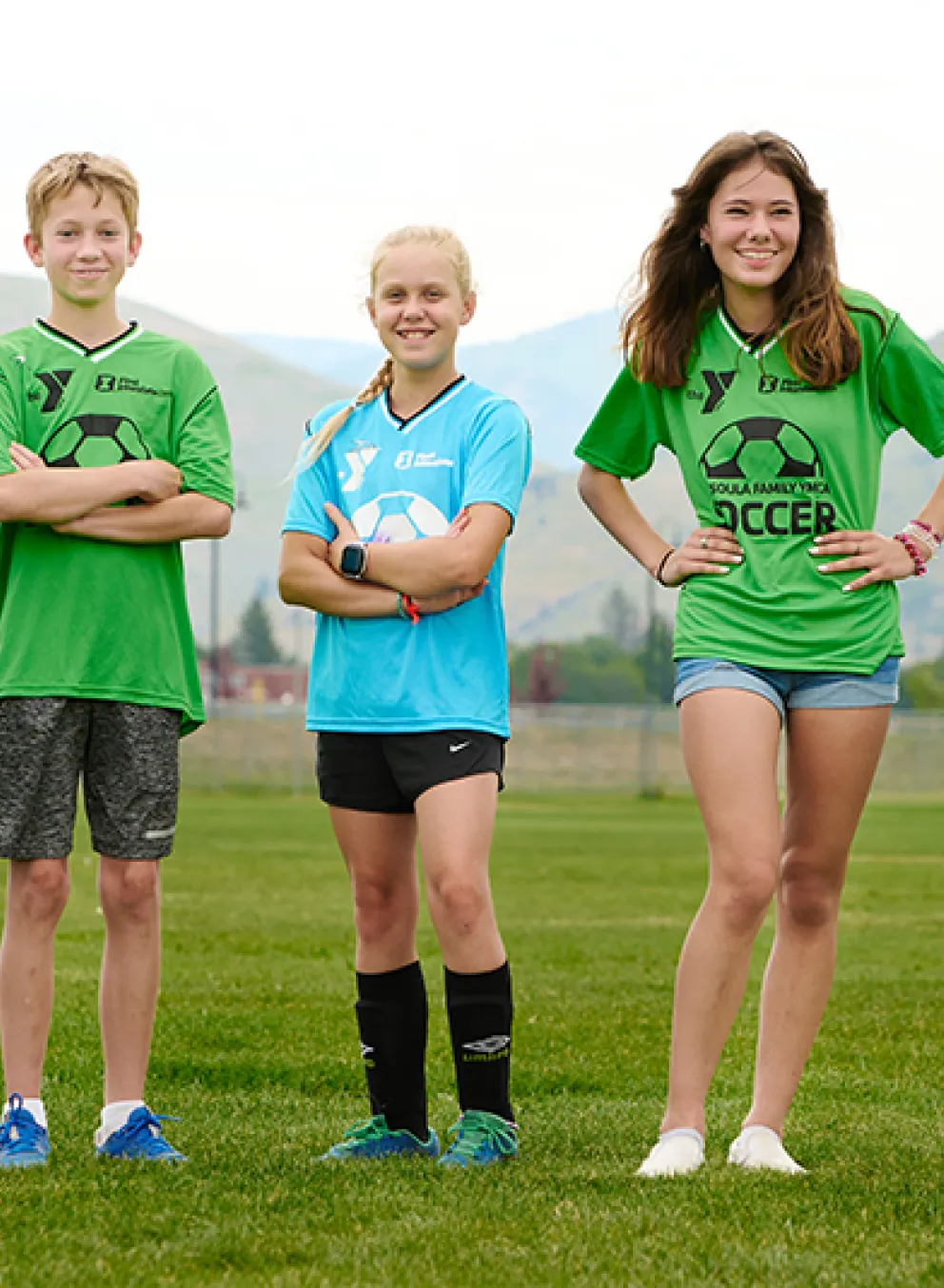 four youth soccer players in soccer jerseys standing on the field with their arms crossed and smiling