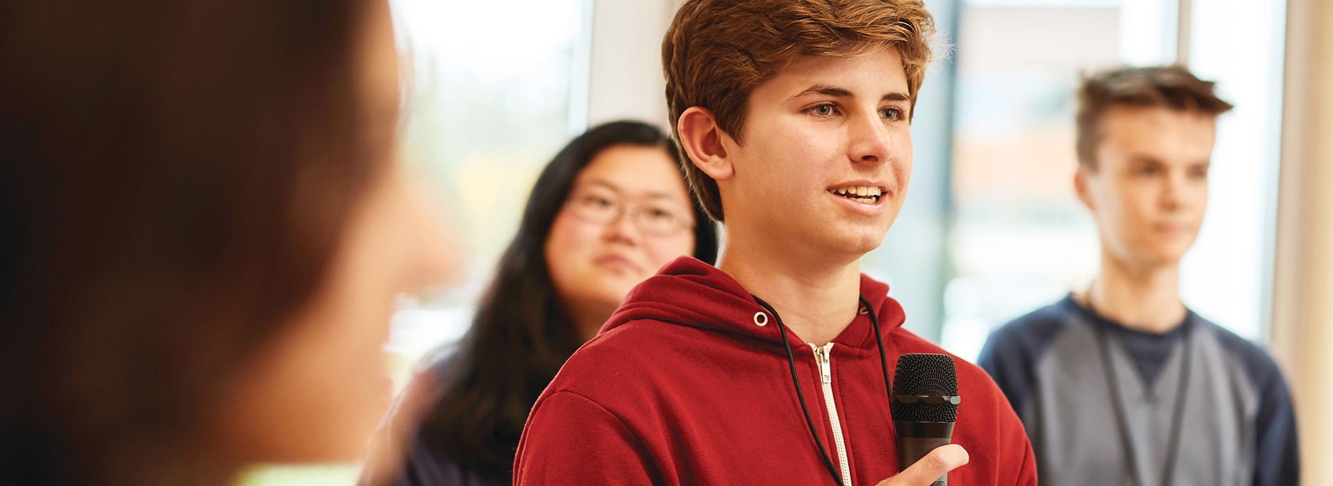 a teenager speaking into a microphone and presenting to other teenagers