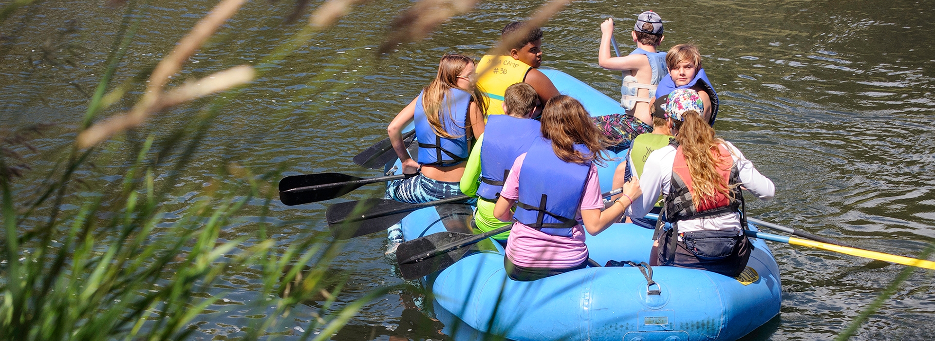 a group of summer campers in lifejackets rafting down a gentle river