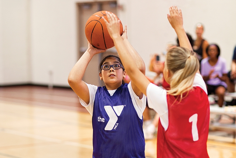 two teens in jerseys playing basketball against one another inside a gym.