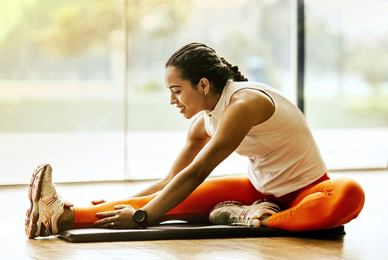 an adult in leggings and tennis shoes stretching on a workout mat