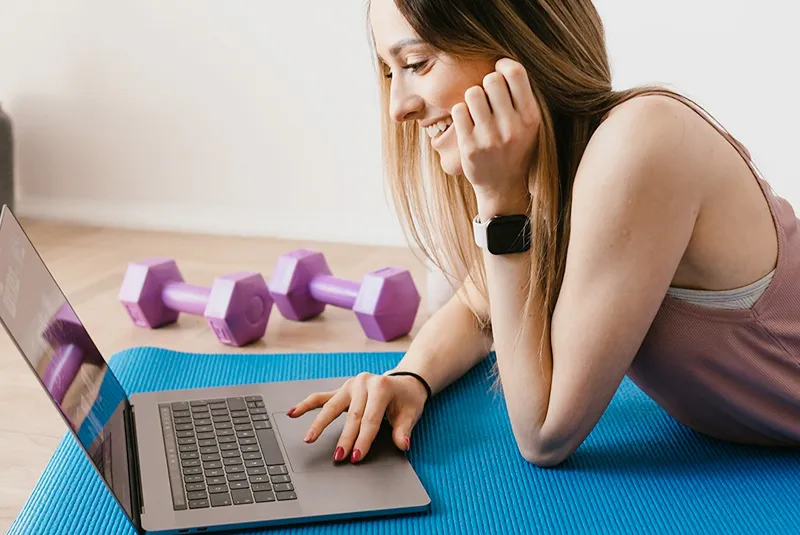 a woman in workout clothes on her laptop and getting ready to do an online fitness class.