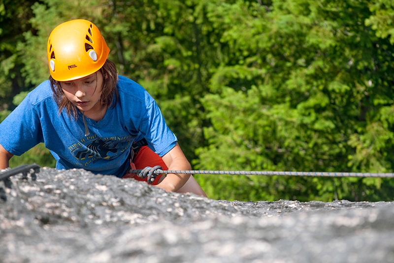 a teen in yellow helmet is rock climbing outdoors