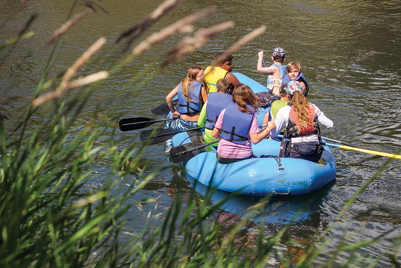 the backs of a group of teens rafting down a gentle river