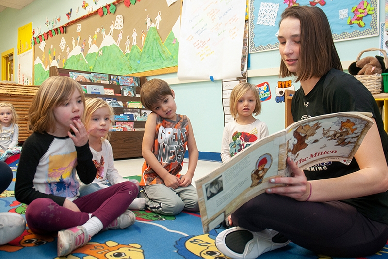 a teenager reads a book to young children in a preschool classroom