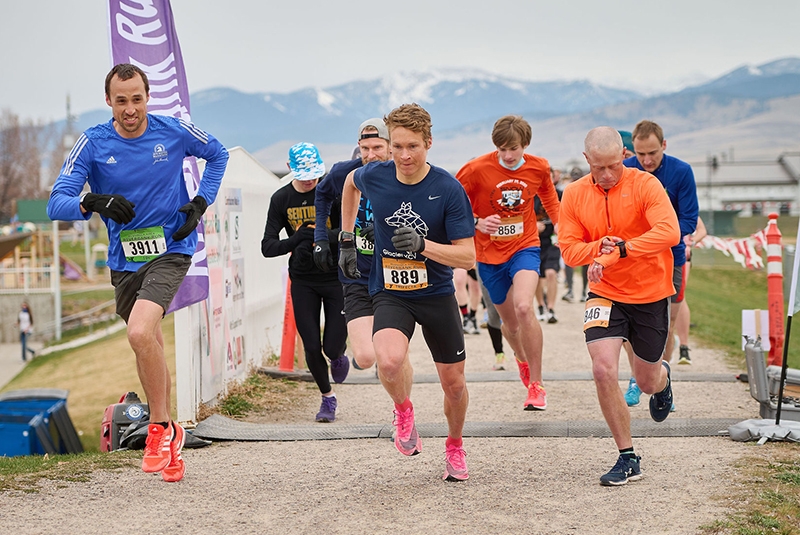 adults wearing race bibs taking off at the startline of a running race. it is a cloudy day.