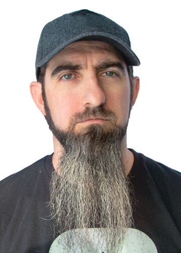 headshot of a man with along grey and black beard and a baseball hat looking serious