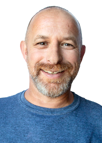 headshot of a smiling man with a grey and red beard and wearing a blue shirt