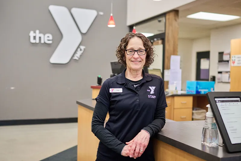 YMCA staff member stands in front of desk smiling