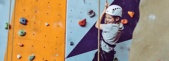 a child in a white helmet climbing on a colorful indoor rock climbing wall