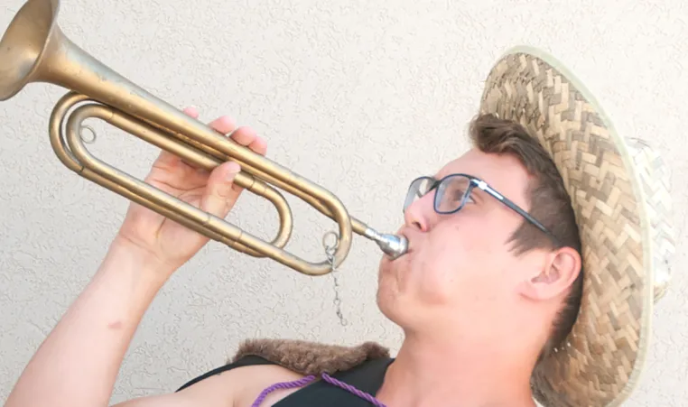 young adult with glasses and a straw hat pretending to play a trumpet 