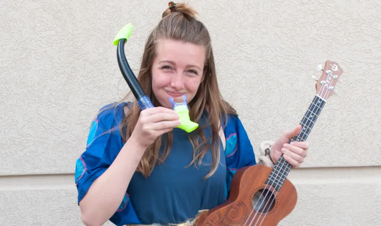 a young woman with long brown hair and a blue shirt holding a snorkle and a ukelele